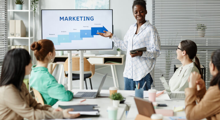 African young businesswoman pointing at monitor and presenting her report to colleagues at business presentation at office